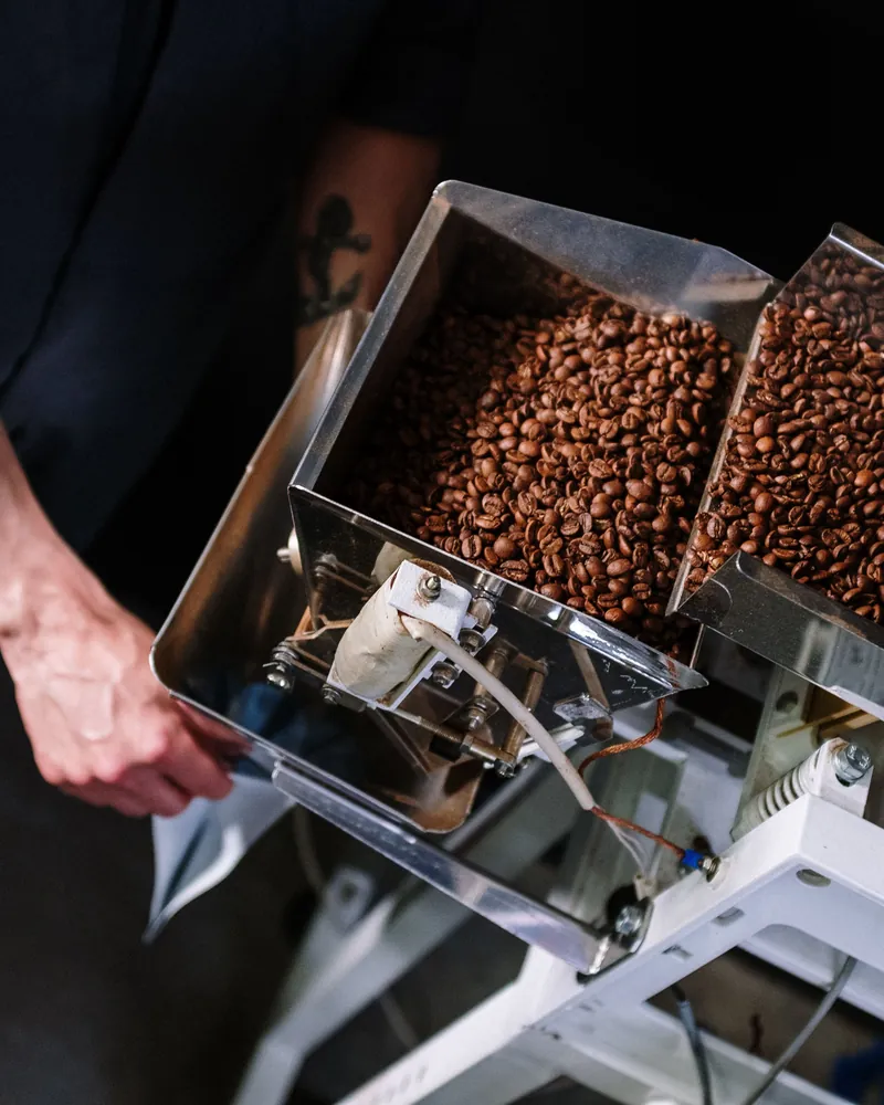Les grains torréfiés passent dans la doseuse en inox, un sachet tenu sous la sortie